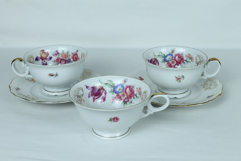 Set of three floral teacups and saucers on a white background