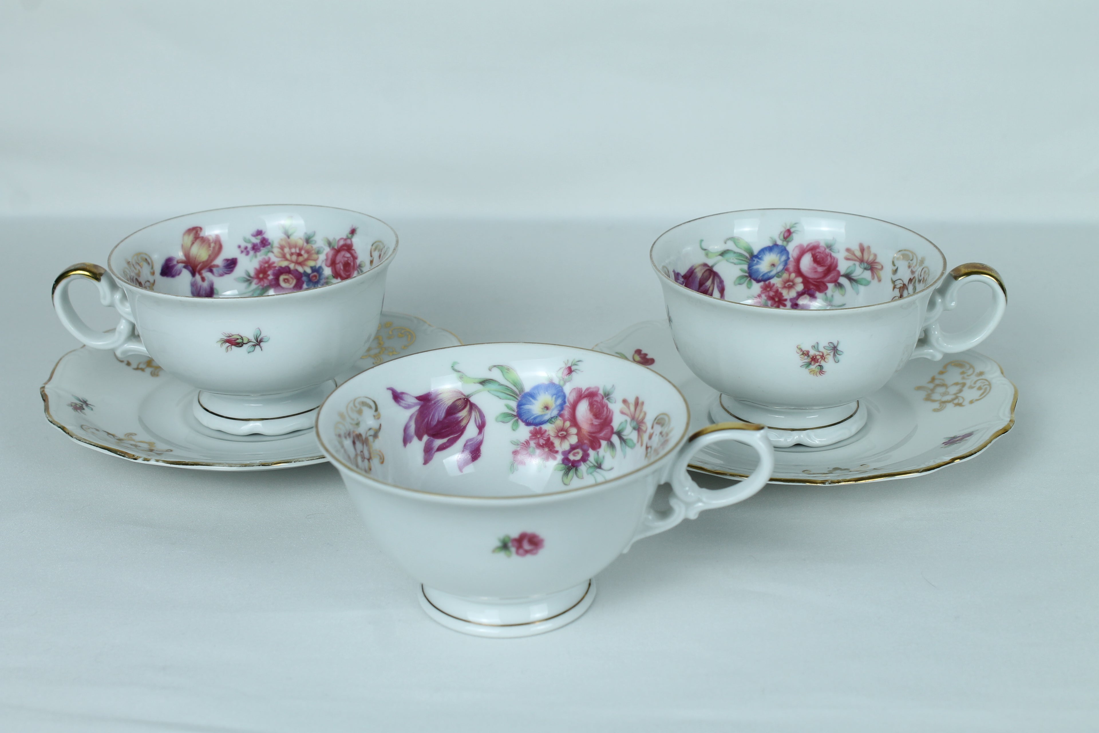 Set of three floral teacups and saucers on a white background