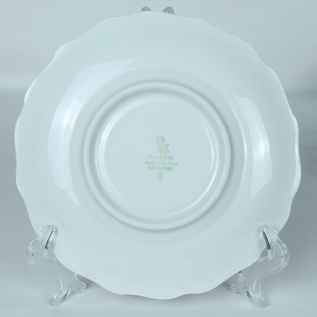 White ceramic plate with a decorative rim on an acrylic stand against a light gray background