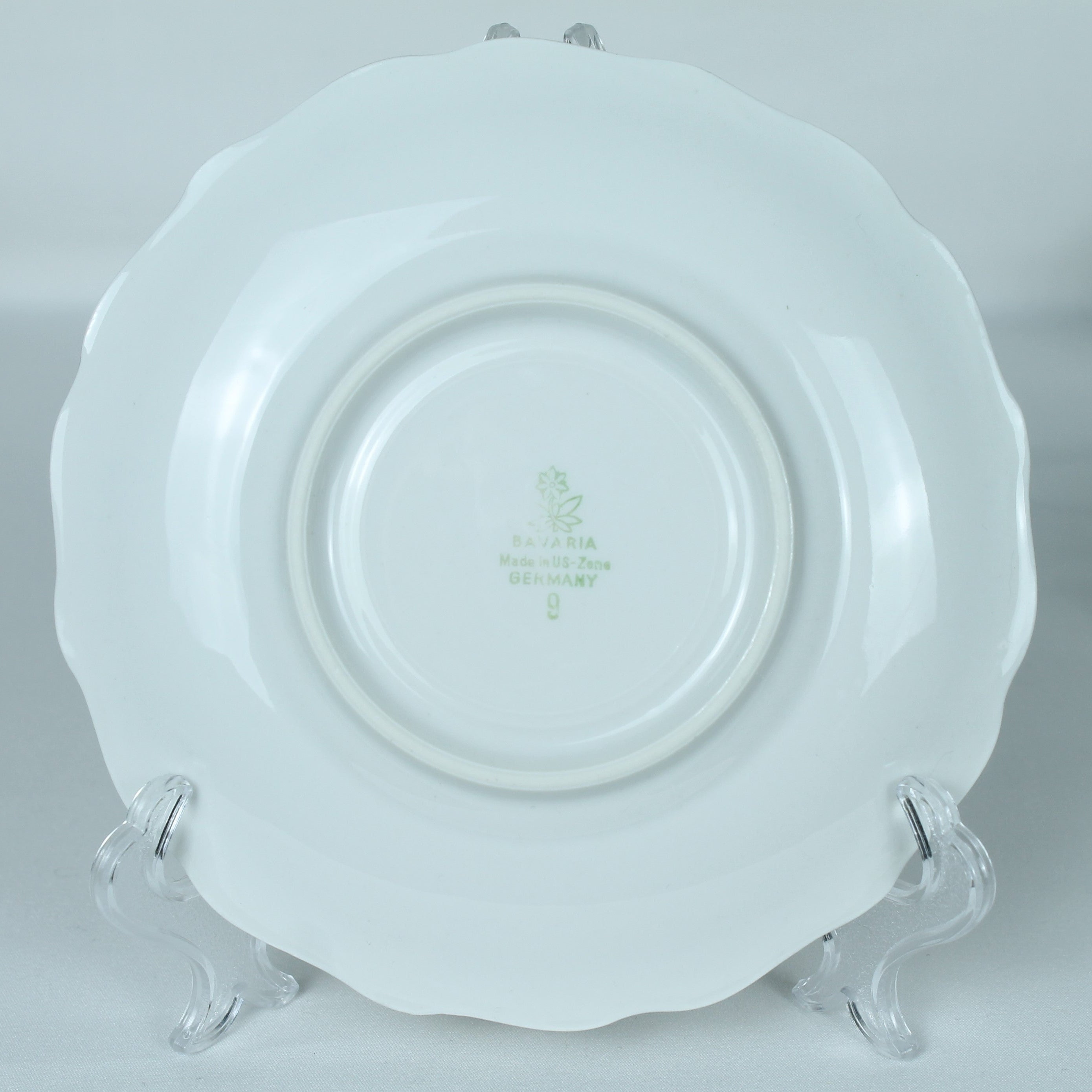 White ceramic plate with a decorative rim on an acrylic stand against a light gray background