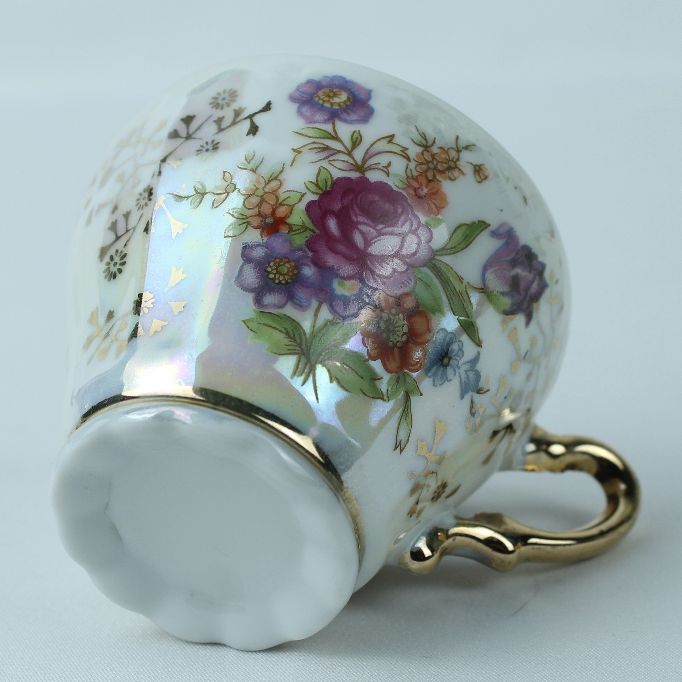 Ceramic mug with floral design and gold handle on a light gray background