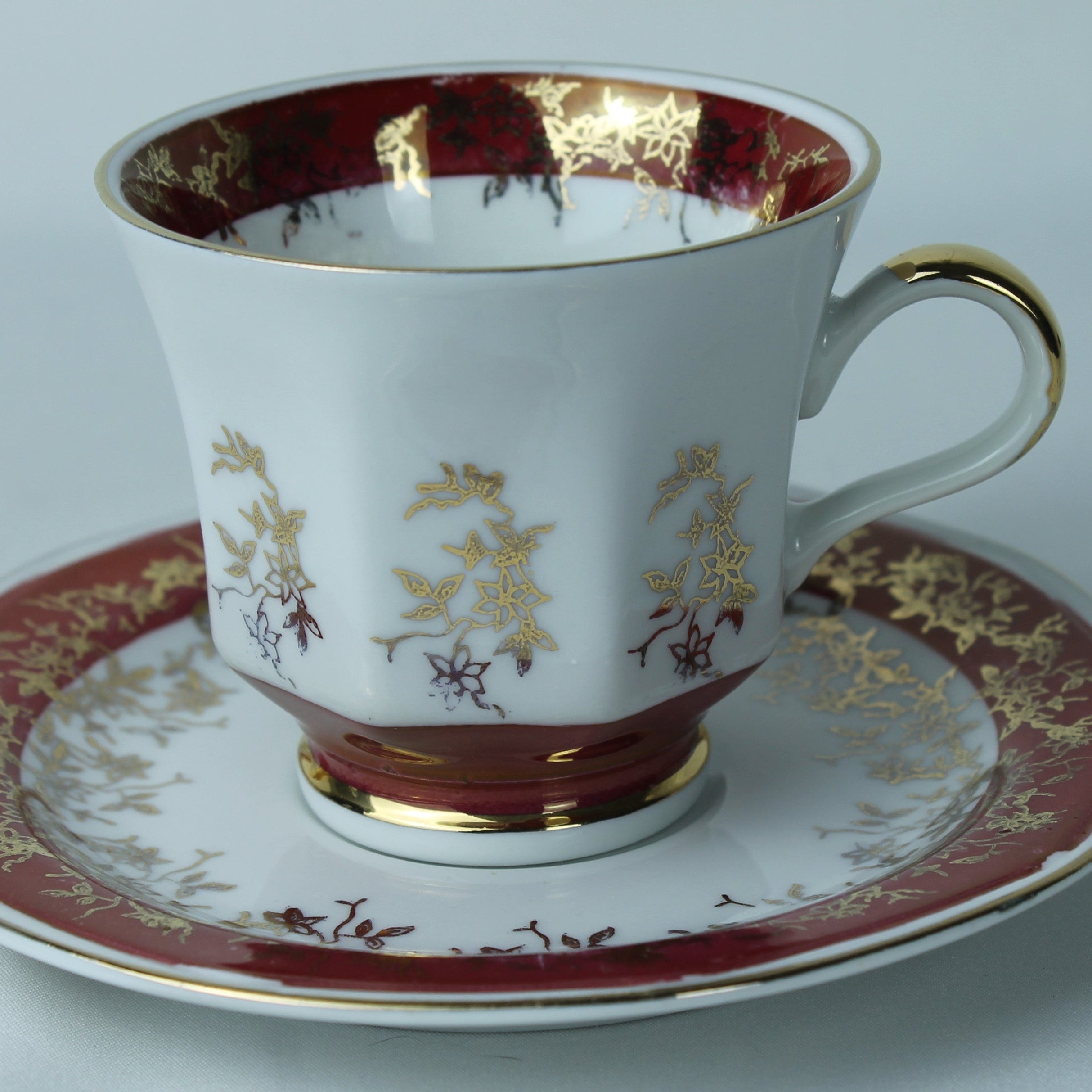 Decorative teacup and saucer with gold and red patterns on a white background