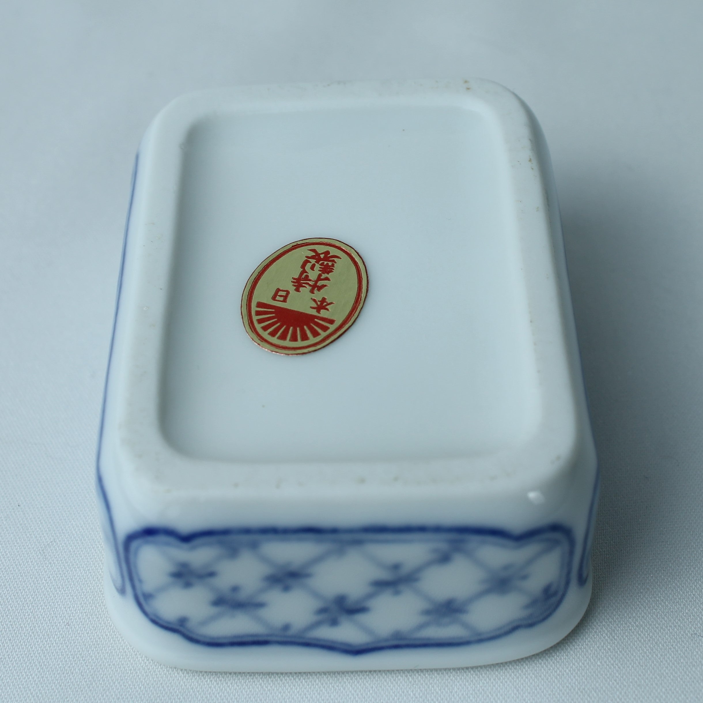 Rectangular white ceramic container with blue patterns and a red logo on a light gray background