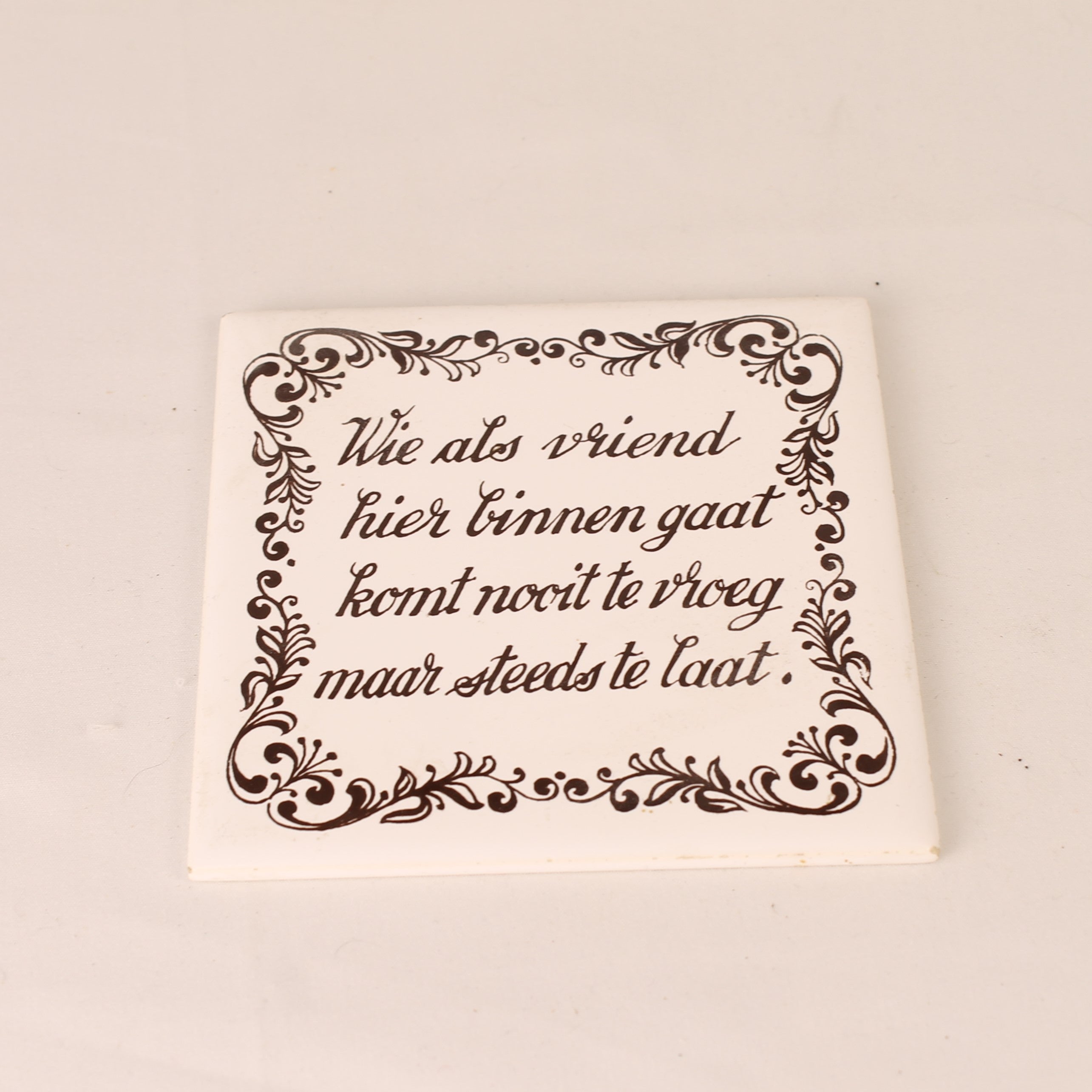 Square ceramic tile with decorative text and border on a beige background