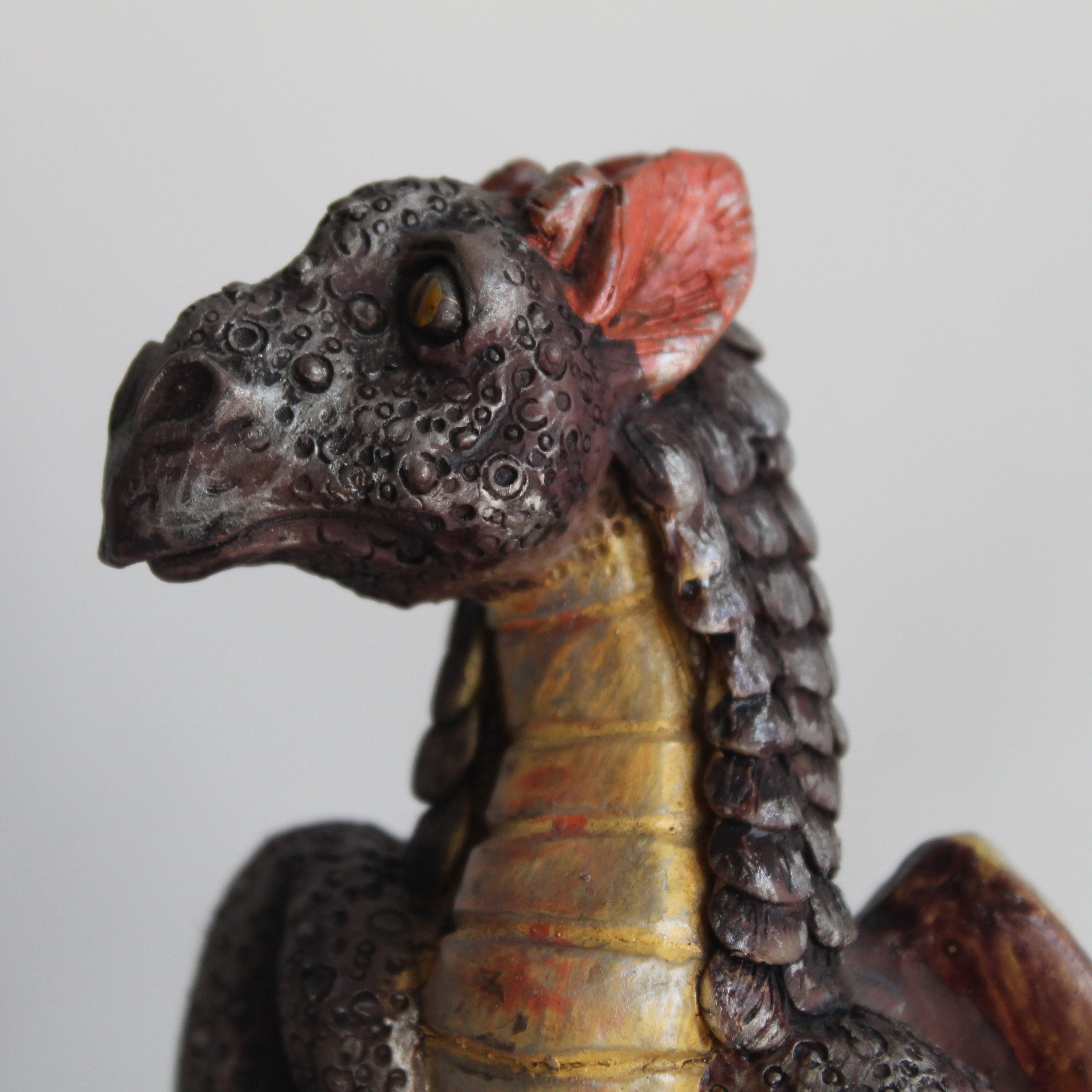 Close-up of a detailed dragon figurine with a textured head and wings on a plain background