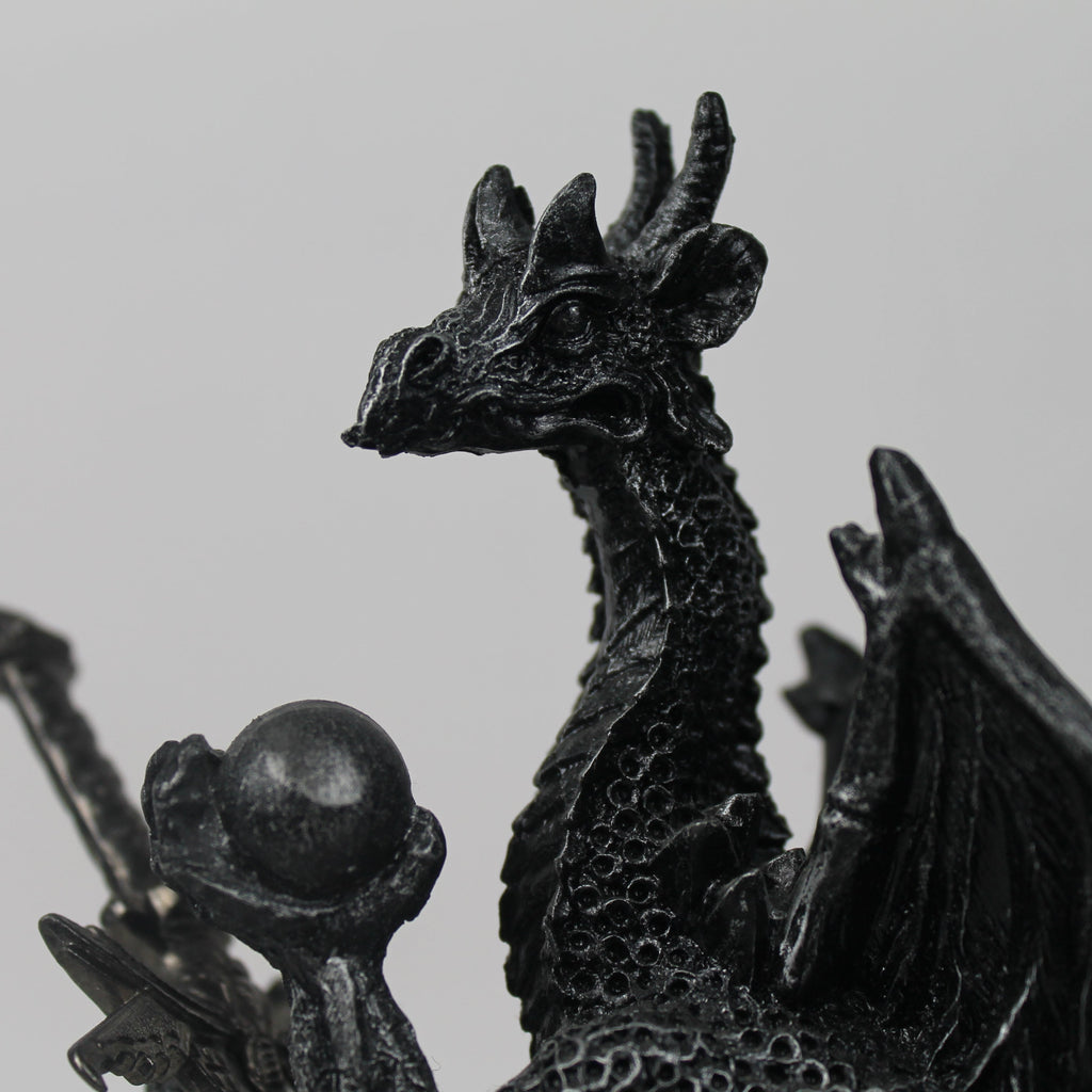 Black dragon figurine with a sphere on a gray background