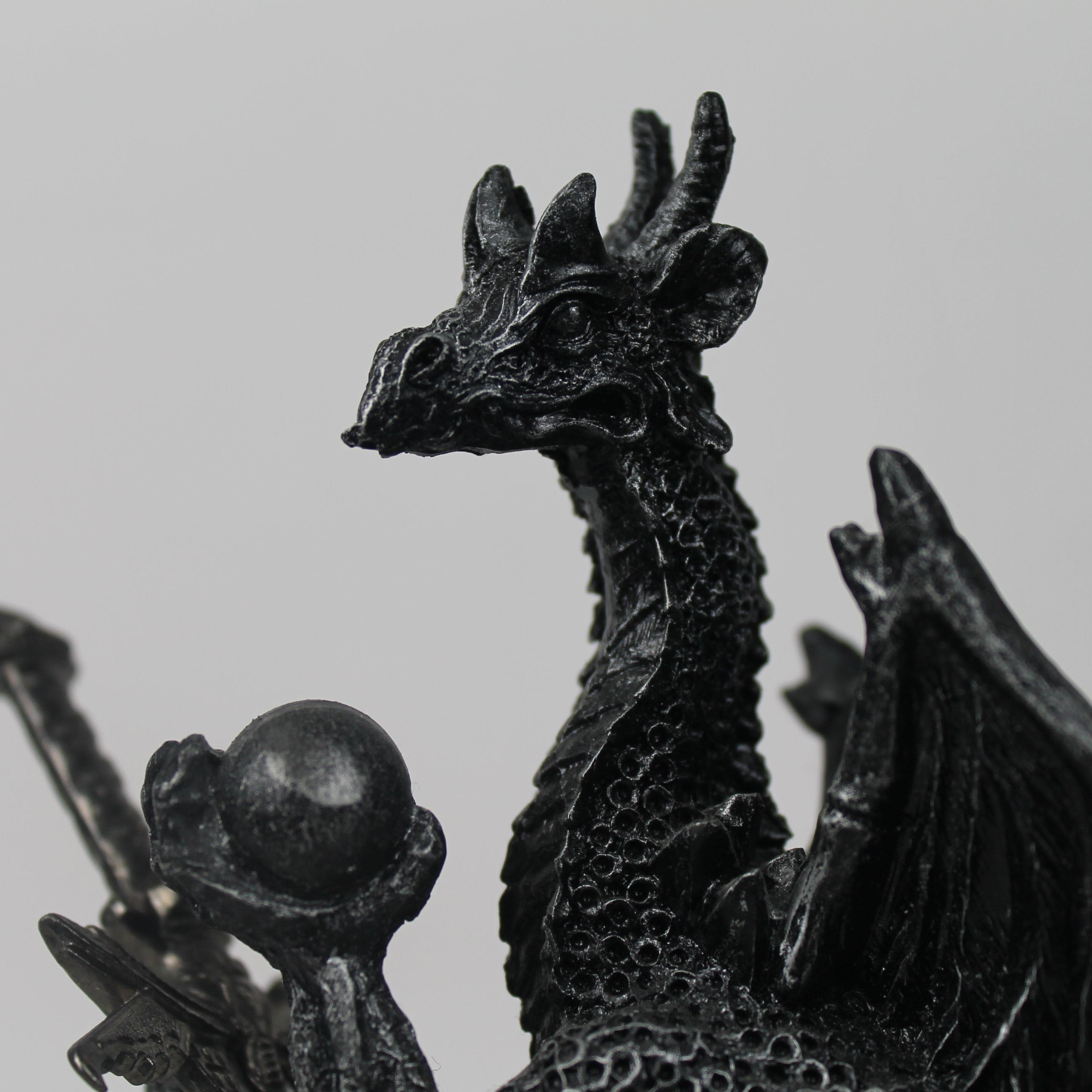 Black dragon figurine with a sphere on a gray background