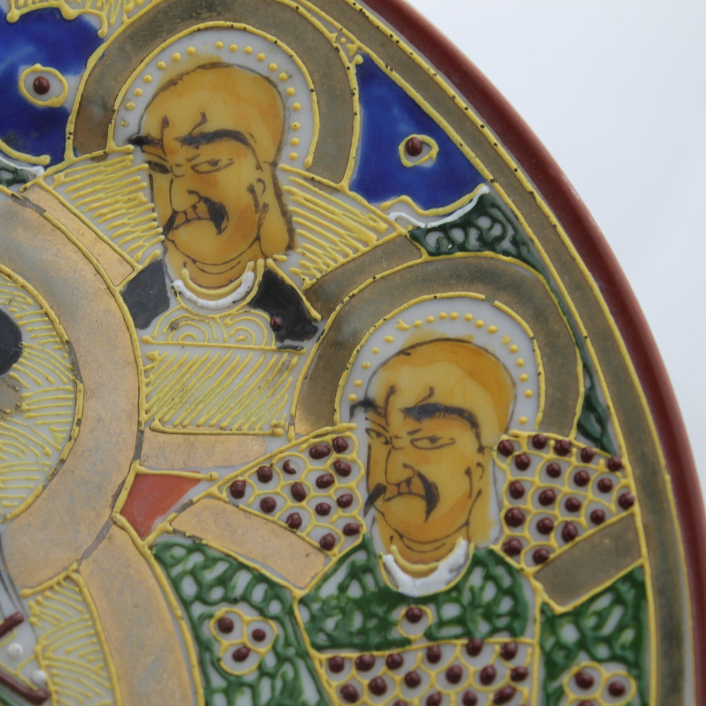 Decorative plate with enameled portraits of three figures against a blue sky.