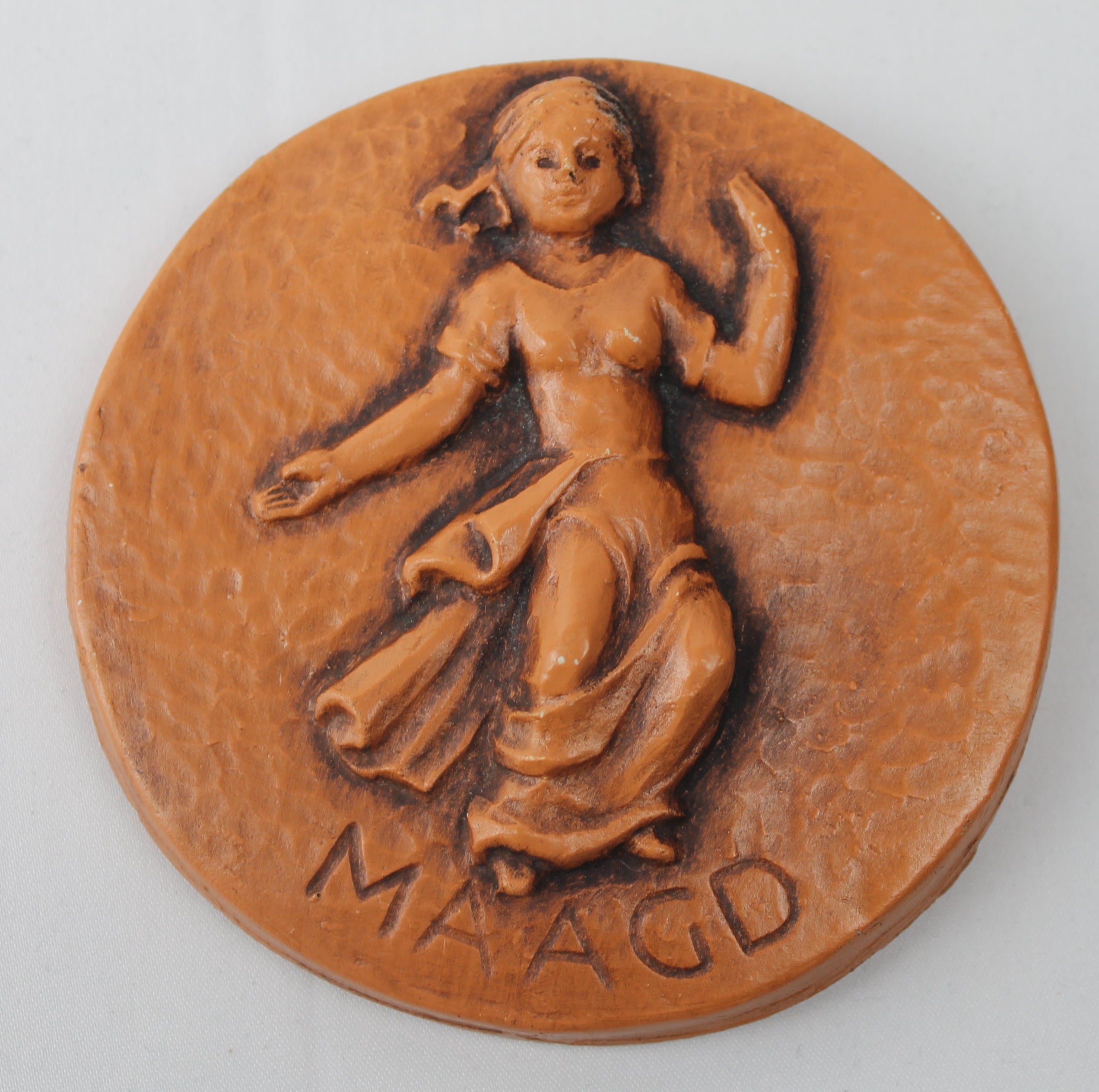 Terracotta plaque with a woman's figure and 'MAAGD' inscription on a white background