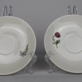 Two white saucers with floral decorations on stands against a gray background