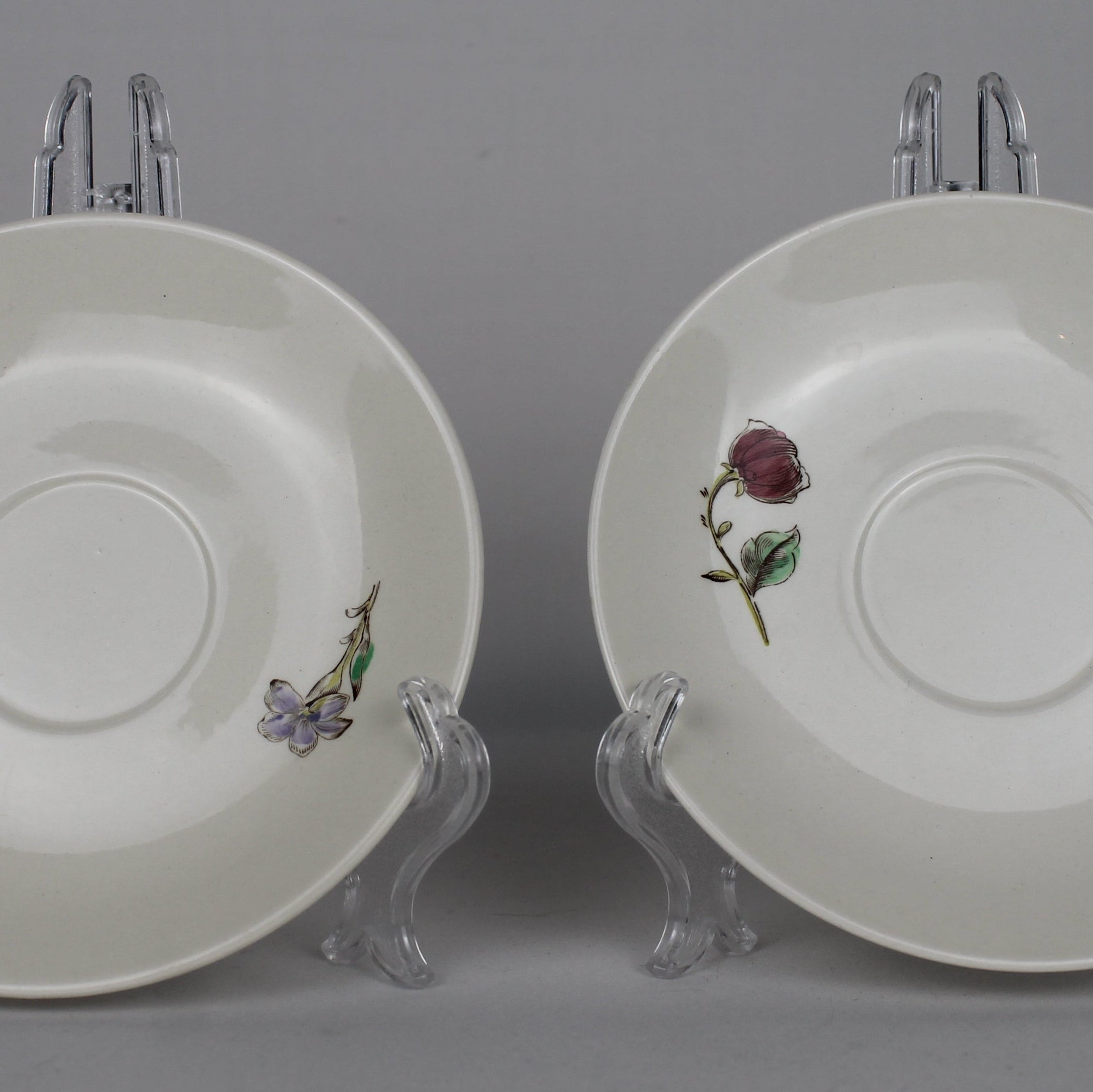 Two white saucers with floral decorations on stands against a gray background