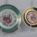 Two decorative plates with classical scenes on stands against a gray background