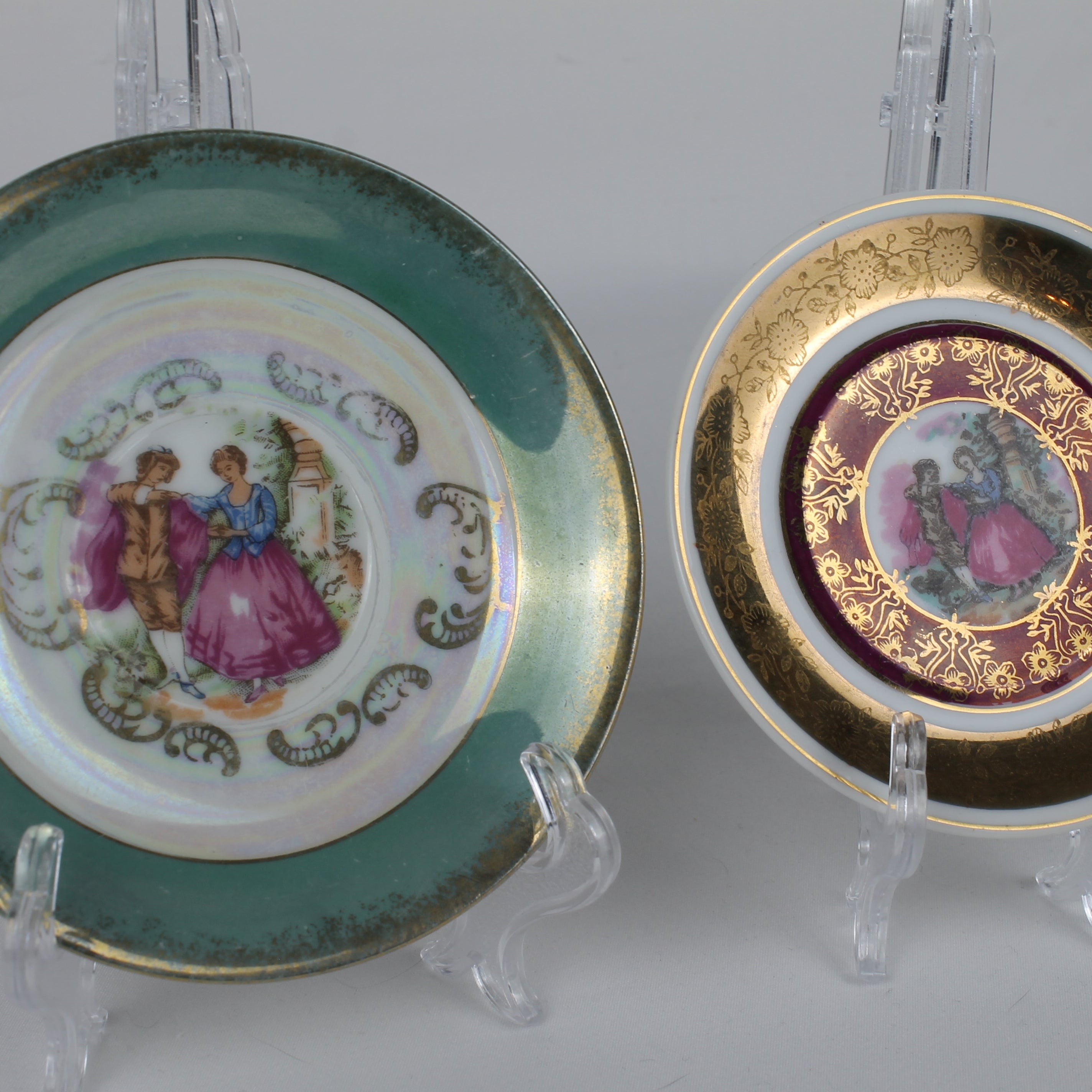 Two decorative plates with classical scenes on stands against a gray background