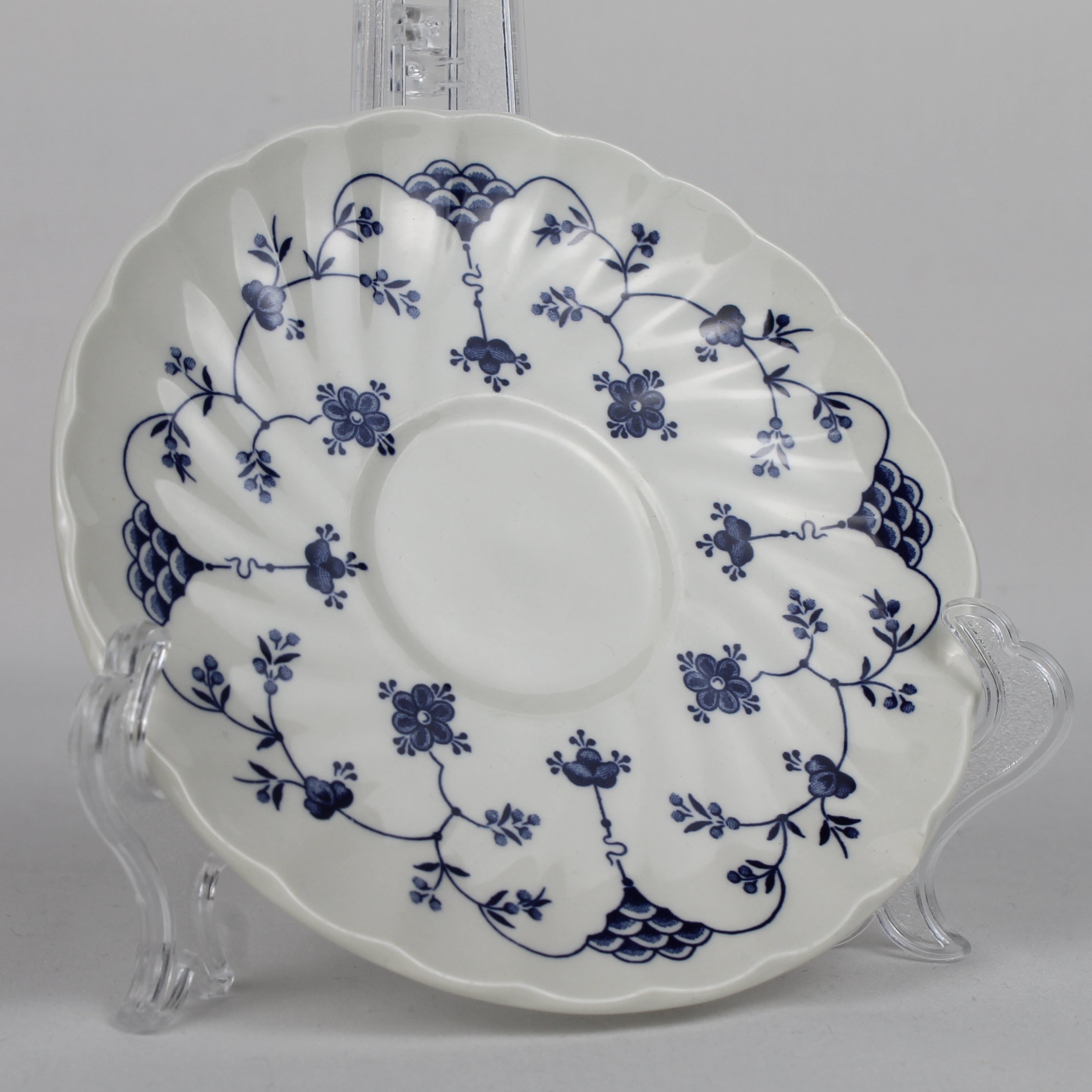 White ceramic plate with blue floral patterns on a clear stand against a gray background