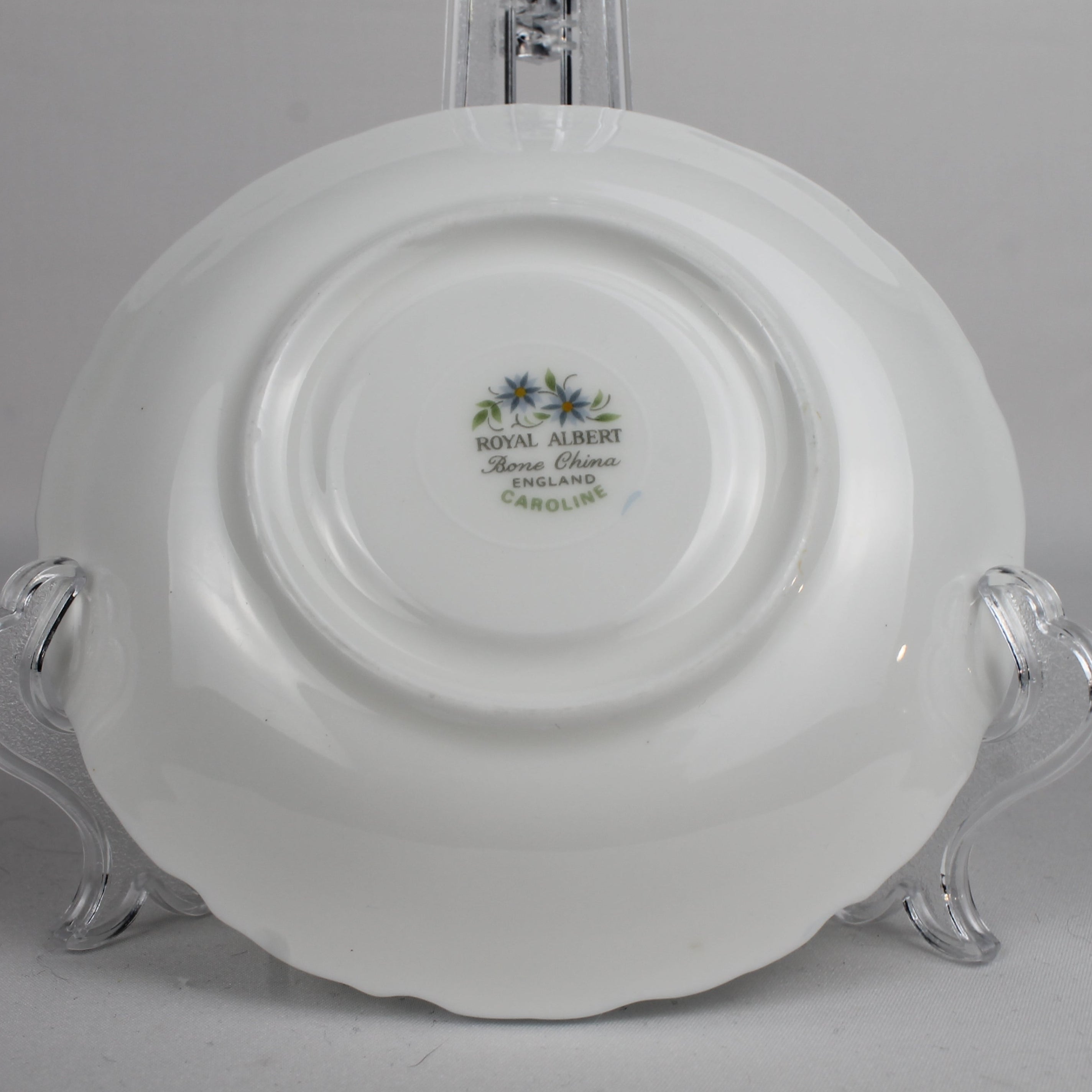 White ceramic plate with 'Royal Albert' branding on a clear stand against a gray background