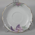 White ceramic saucer with purple floral design on a clear stand against a gray background