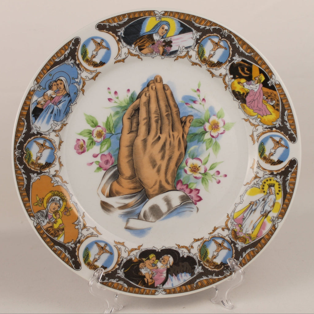 Decorative plate with praying hands and religious scenes on a white background