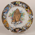 Decorative plate with praying hands and religious scenes on a white background